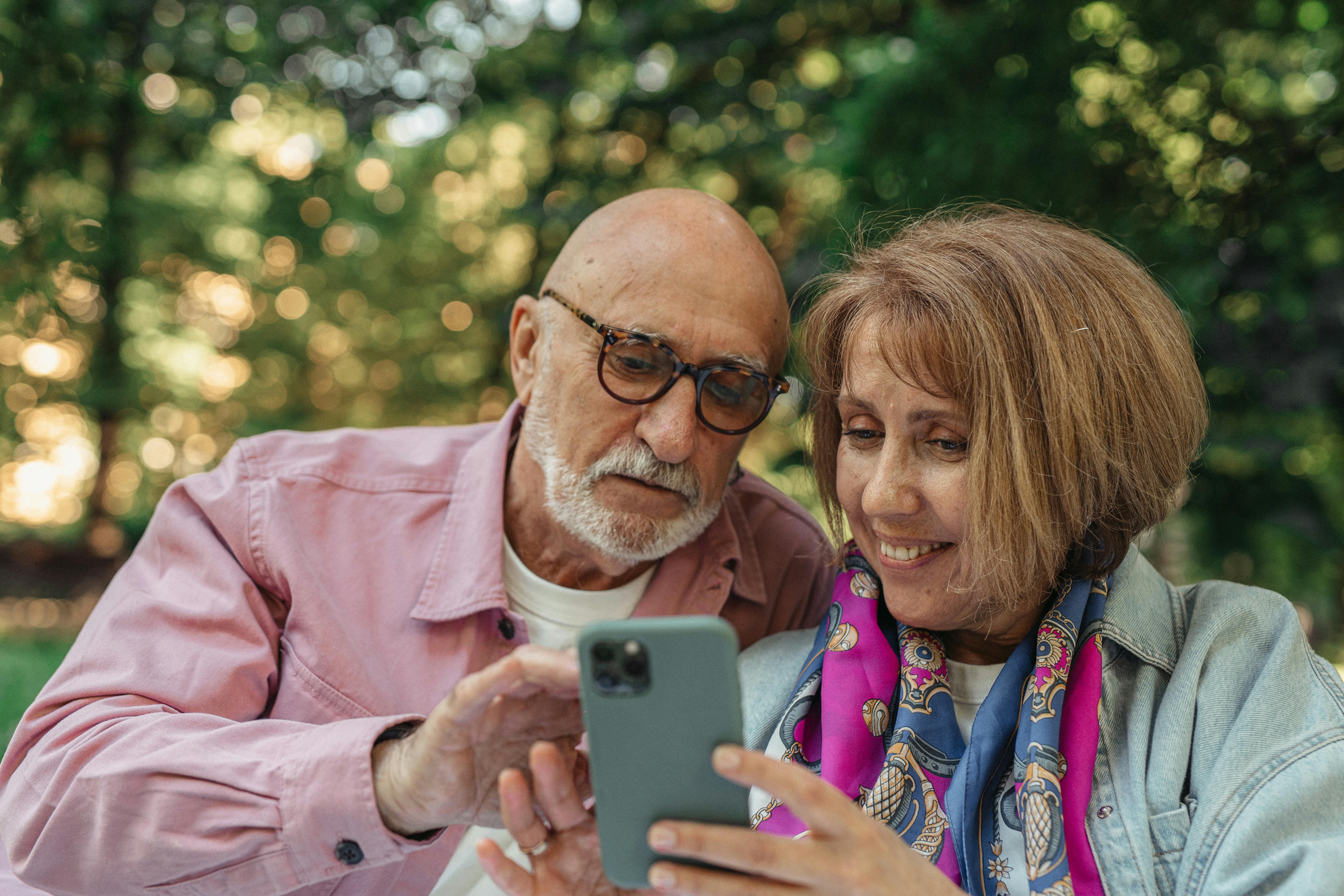 An older couple looking at a phone together outdoors.